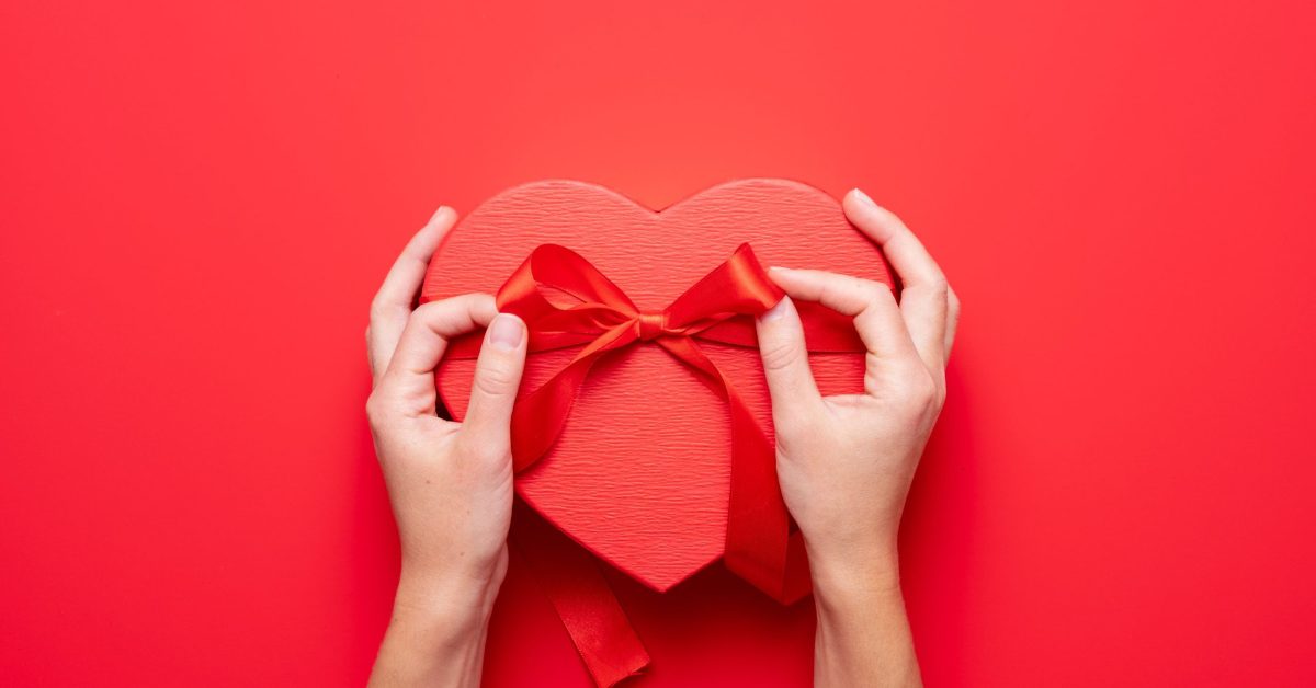 Top view of female hands holding a gift heart shape. Presents for valentine day, birthday, mother's day. Flat lay. Symbol of love. Valentines day background with a gift boxes on concrete board.